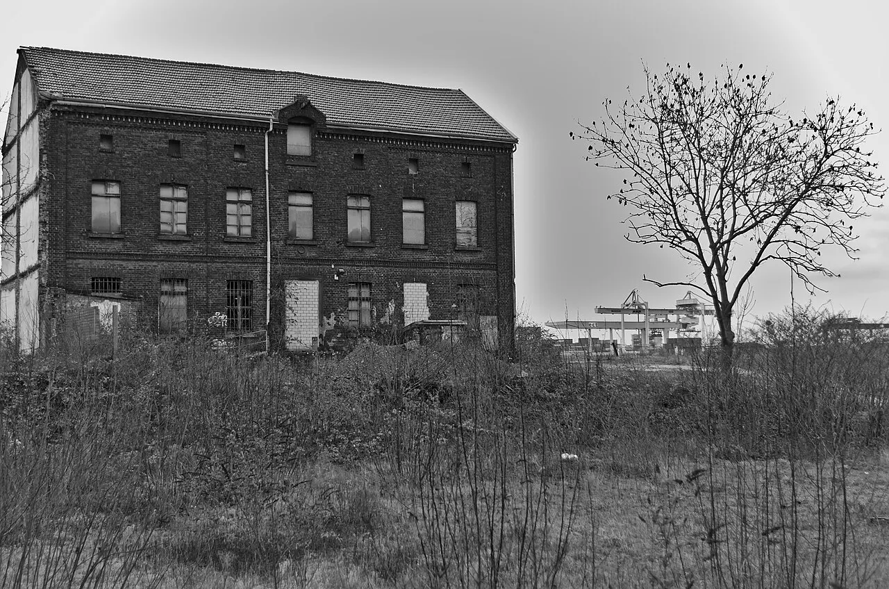 Leerstehendes Backsteingebäude im Ruhrorter Hafen, im Hintergrund die Containerkräne des Duisburger Hafens